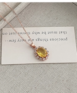 Gros plan d'un collier en or rose avec cristal jaune ovale et halo de diamants