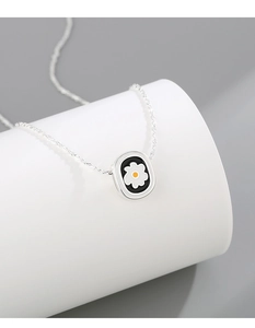 Close-up of a silver daisy necklace with black enamel pendant on a white pedestal