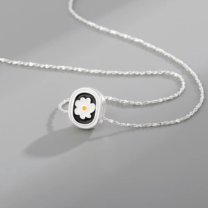 Minimalist silver daisy pendant necklace with a white flower on a black background