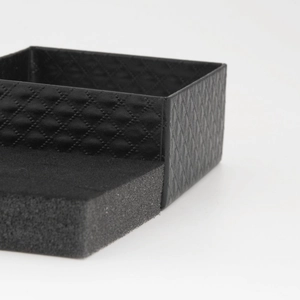 Close-up of a black textured jewelry box with diamond pattern and soft gray foam insert