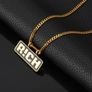 Détail du pendentif RICH doré avec incrustation noire et chaîne cubaine plate sur cuir