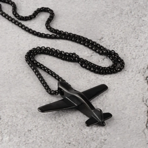 Primer plano de un collar con colgante de avión negro mate sobre fondo gris texturizado