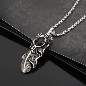 Détail macro du pendentif plume en acier vintage avec pierre noire et chaîne