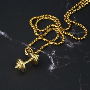 Detail of a golden dumbbell pendant on a round bead chain over black marble background