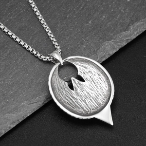 Macro shot of silver eagle eye pendant with box chain on dark rocky background