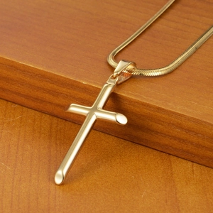 Collier avec pendentif croix dorée et chaîne serpent présenté sur un support en bois