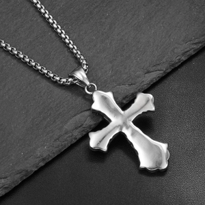 Détail du pendentif croix à texture de lave sur une chaîne box en acier inoxydable