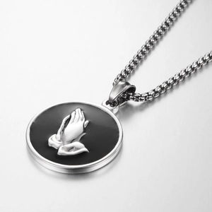Macro shot of silver praying hands relief on black circular pendant with bead chain