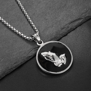 Macro shot of hip hop praying hands pendant necklace on dark gray textured rock