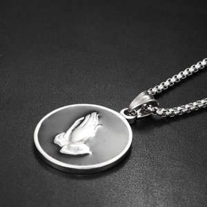 Macro shot of silver hip-hop pendant with embossed praying hands and dark background