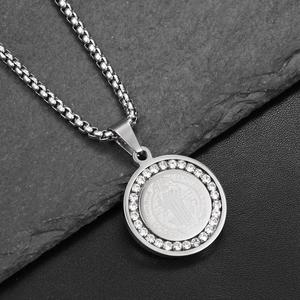 Macro shot of silver St. Benedict medal pendant with white rhinestones on black rock