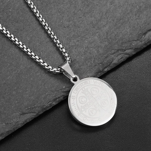 Detail of silver St. Benedict Medal pendant on dark stone background showing fine engraving