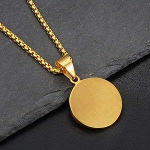 Detail of a polished gold round pendant and box chain on dark textured background
