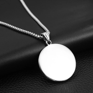 Gros plan du pendentif rond argenté sur chaîne box avec fond en cuir noir texturé