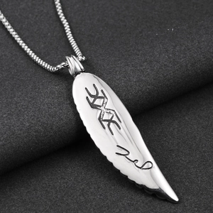 Macro shot of silver titanium steel feather pendant with engraved runes and ball chain