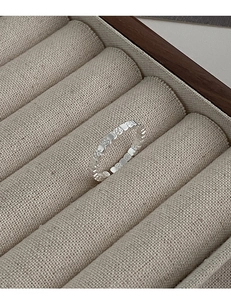 Close-up of minimalist silver geometric texture ring on a beige linen jewelry display