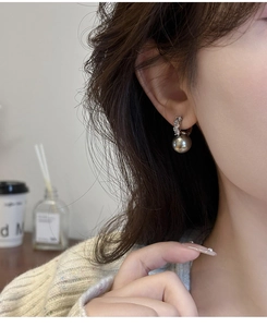 Gros plan d'élégantes boucles d'oreilles perles grises et zircons portées par un mannequin