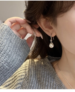 Detailed view of elegant pearl drop earrings with sparkling zircon on model in grey sweater