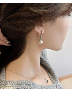 Close-up of elegant pearl drop earrings worn by a model with a grey knit sweater