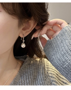 Detail of silver drop earring with round white pearl and sparkling zircon on a model