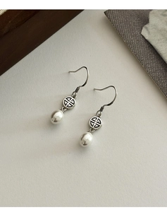 Dettaglio macro degli orecchini di perle con decori a volute in argento e ganci