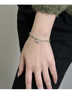 Detail of silver bamboo joint bracelet with green jade beads and small bells on wrist