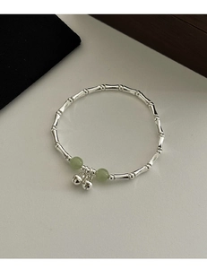 Macro detail of silver bamboo-style bracelet with green jade-like beads and small bells