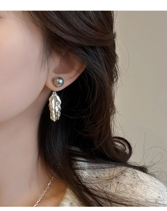 Détail de boucles d'oreilles avec perle et pendentif feuille portées par un mannequin