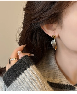 Detail of heart stud earrings with silver wing drops worn by a model in knitwear