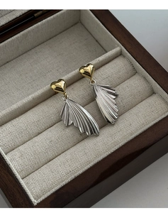 Close-up of gold heart stud earrings with silver wing pendants in a luxury wooden box
