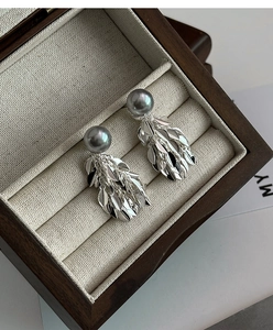 Détail de boucles d'oreilles feuilles argentées avec perle grise sur tissu beige