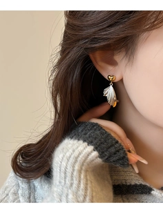 Detail of elegant gold heart and silver wing earrings worn by a model on grey knitwear