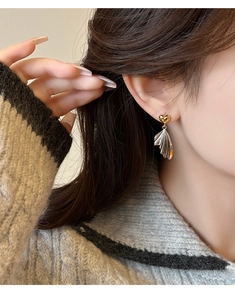 Detail of French heart wing earrings with gold and silver metallic textures on a model