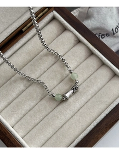 Close-up of bamboo-shaped jade pendant with silver chain in a wooden jewelry box