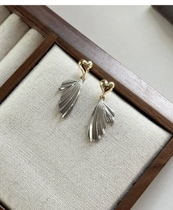 Close-up of gold heart stud earrings with silver pleated wing dangles on linen tray