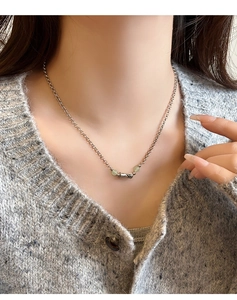 Close-up of a silver bamboo-style necklace with green jade beads on a model wearing knitwear