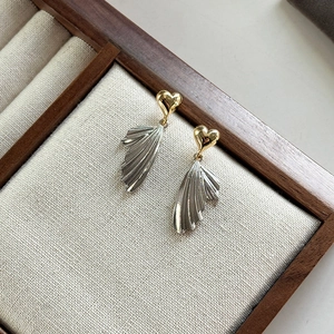 French style heart and wing stud earrings in gold and silver finish on linen background