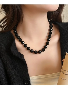 Gedetailleerd beeld van gepolijste zwarte onyx kralenketting op een model met minimalistische kleding