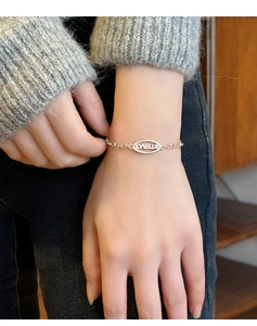 Gros plan d'un bracelet minimaliste en argent avec pendentif ovale LOVEME porté au poignet