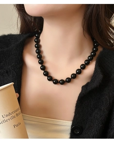 Detailopname van zwarte onyx kralenketting gedragen door een model over een zwart vest