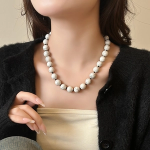 Minimalistische witte turquoise kralenketting met marmeren textuur op zwarte trui