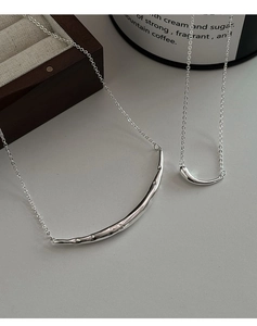 Détail de deux colliers minimalistes avec pendentifs incurvés au fini argenté
