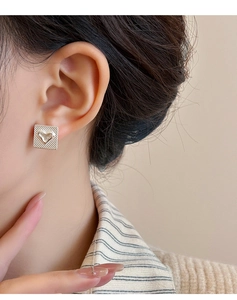 Détail macro d'une boucle d'oreille carrée dorée avec cœur 3D sur base quadrillée