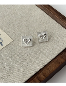 Gros plan de clous d'oreilles en argent avec motifs à carreaux et détails cœur
