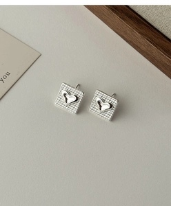 Détail de boucles d'oreilles carrées argentées avec motif à carreaux et cœur central