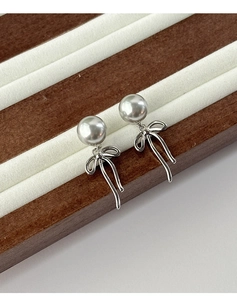 Detail of silver bow and white pearl drop earring on elegant velvet display tray