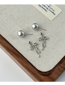 Detail of elegant grey pearl earrings and silver ribbon bow studs on canvas display