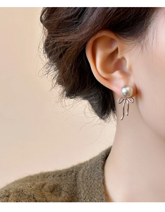 Close-up of elegant grey pearl earrings with silver ribbon bow pendant on female ear