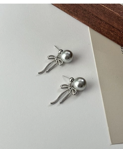 Detail of silver bow and grey pearl drop earrings on minimalist white background