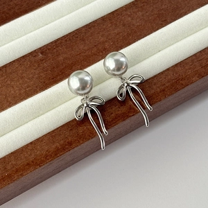 Elegant silver bow earrings with large white pearls displayed on a premium white velvet tray